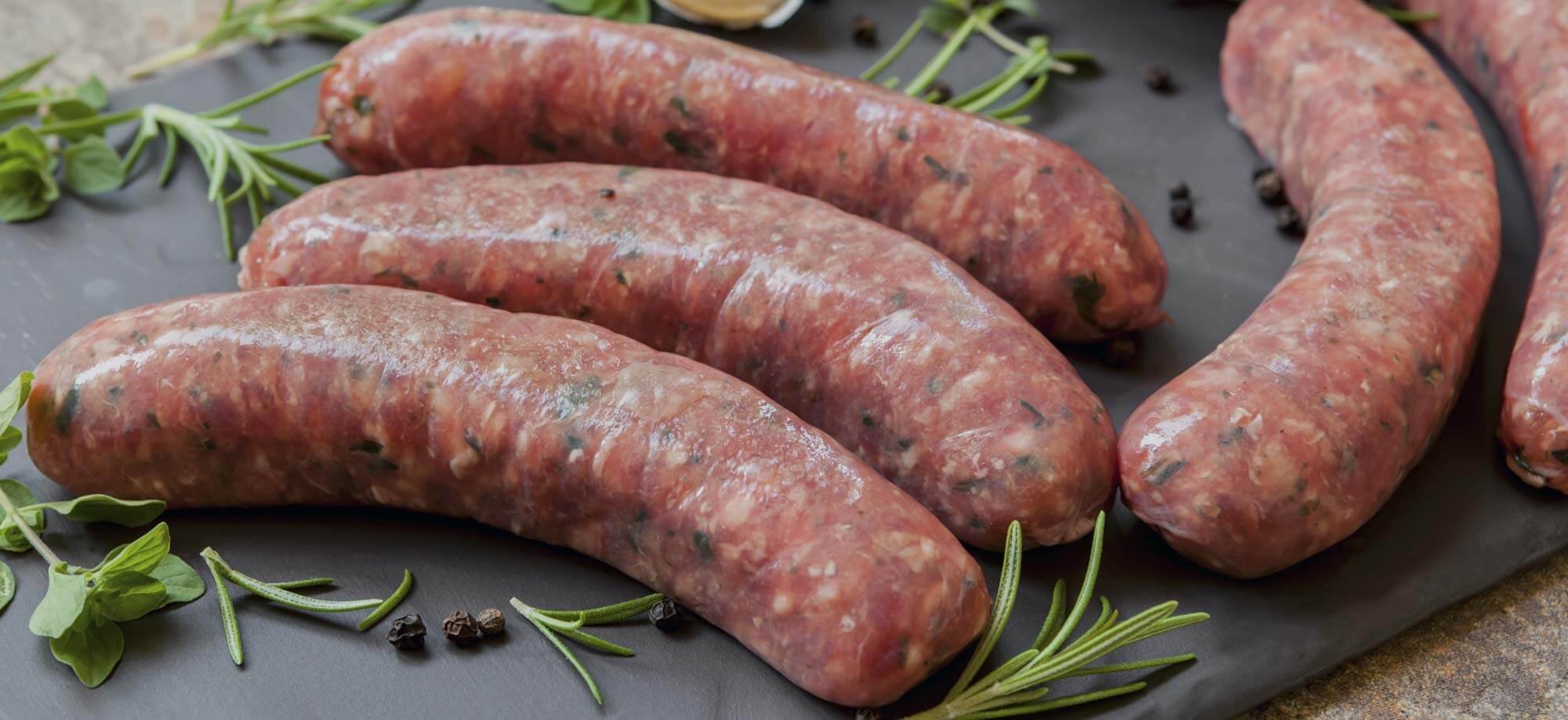 Wild Rice Brats laying on a cutting board with spices and green garnish